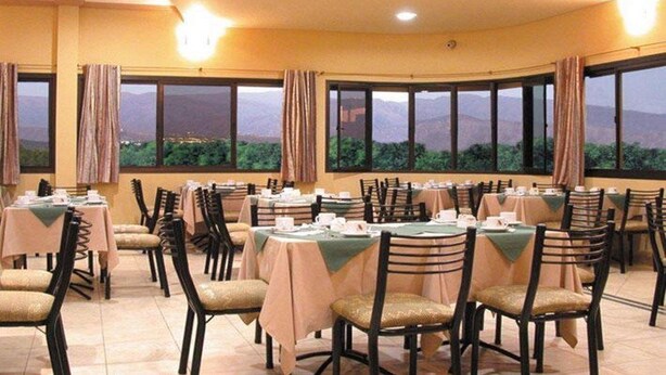 A dining area with tables set for service, large windows with curtains, and a view of mountains. - Alcor Hotel (Mendoza)