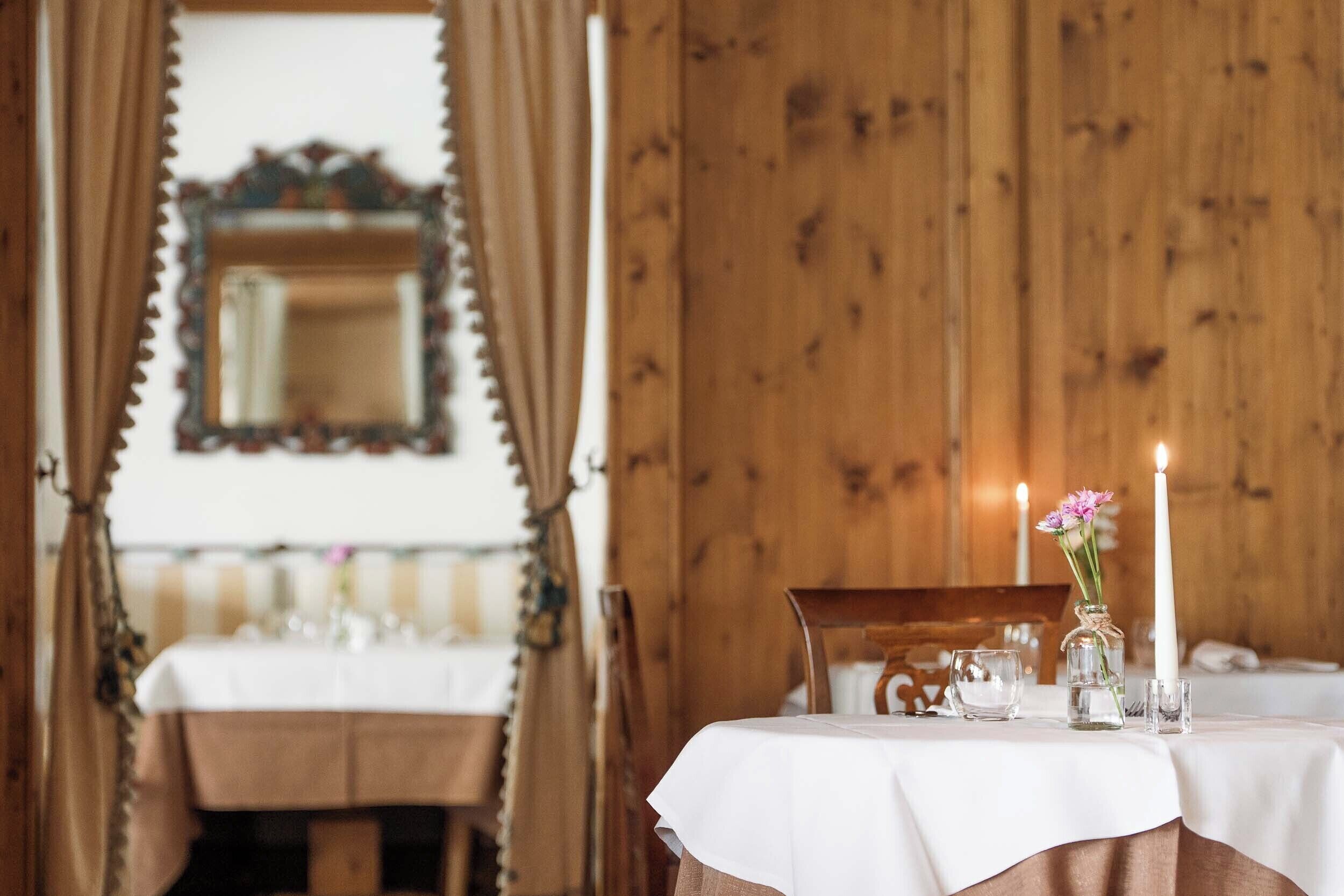 A dining table with a white tablecloth, a candle, and a vase with flowers.