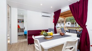A dining area with a white table, red curtains, and a bowl of fruit. - Mobile Homes Adriatic Camping Bi Village (Fazana)