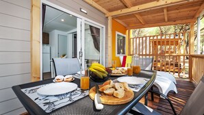 A covered outdoor dining area with a table set for breakfast, including bread, fruit, and beverages. - Mobile Homes Adriatic Camping Bi Village (Fazana)