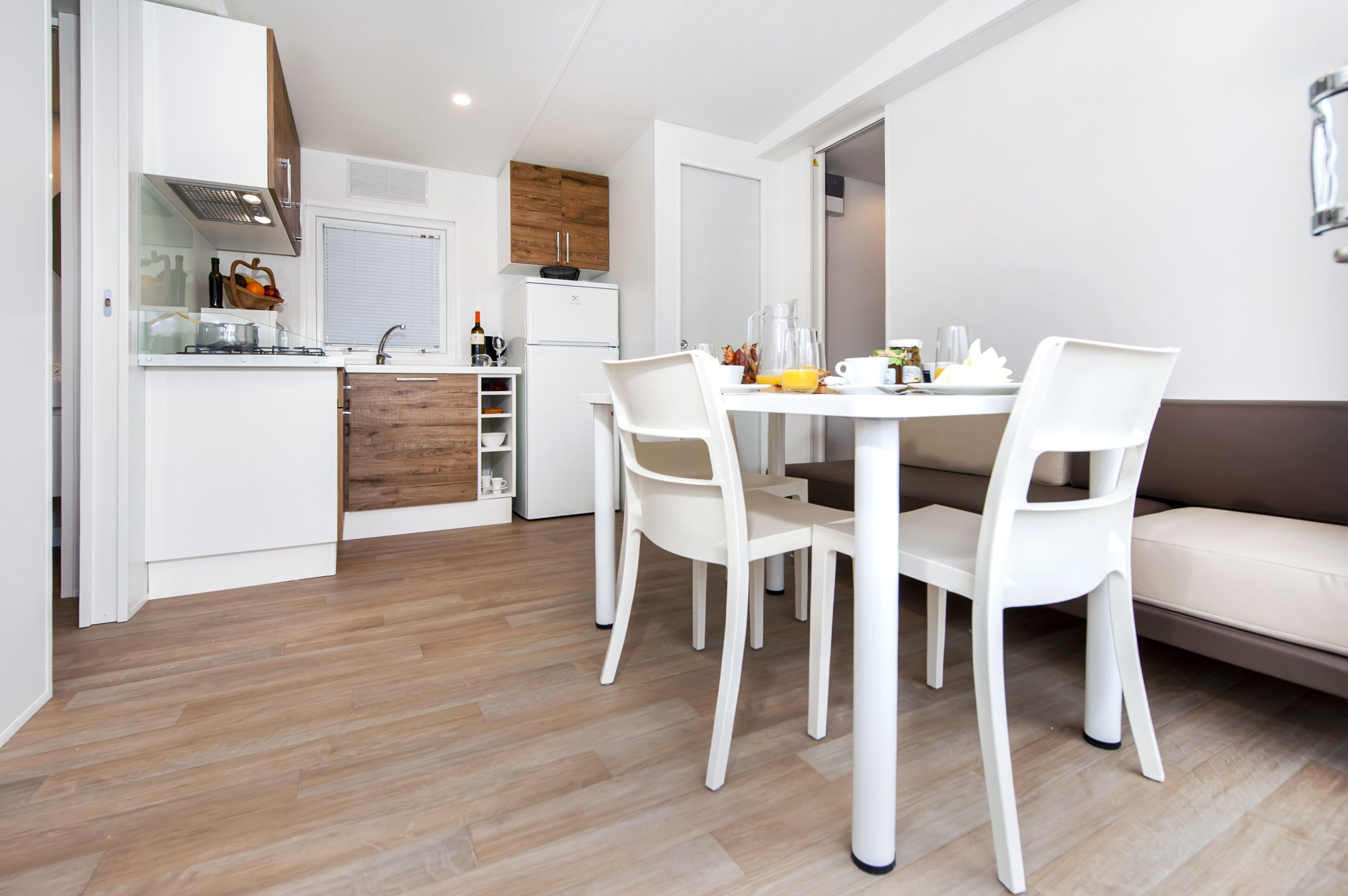 Une cuisine compacte avec des meubles blancs, un plan de travail en bois et un coin repas comprenant une table et des chaises blanches.
