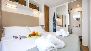 A neatly made bed with white linens, a green tray with orange juice and croissants, and rolled white towels. - Mobile Homes Adriatic Camping Bi Village (Fazana)