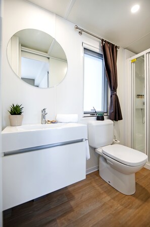 A modern bathroom with a white vanity, a round mirror, a toilet, and a shower area.