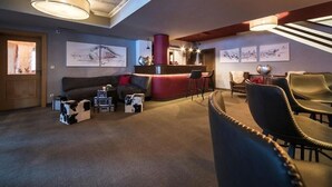 A modern living room with a red accent wall, a black leather sofa, and a coffee table. There are framed artworks on the walls and a large window providing natural light. - Montjola (Sankt Anton am Arlberg)