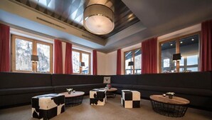 A modern hotel room with a dark-colored sofa, three black and white patterned ottomans, and a round wooden coffee table. - Montjola (Sankt Anton am Arlberg)