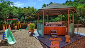 A wooden gazebo with a bench and a hot tub, surrounded by a playground with swings and a slide. - Casa Scopeti (San Casciano in Val di Pesa)