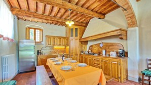 A rustic kitchen with wooden cabinets, a long dining table set for six, and a built-in oven. - Casa Scopeti (San Casciano in Val di Pesa)