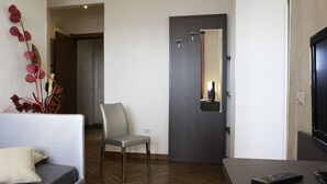 A modern hotel room with a grey sofa, a small table, a TV, and a door with a mirror. - Hotel Astoria (Fermo)