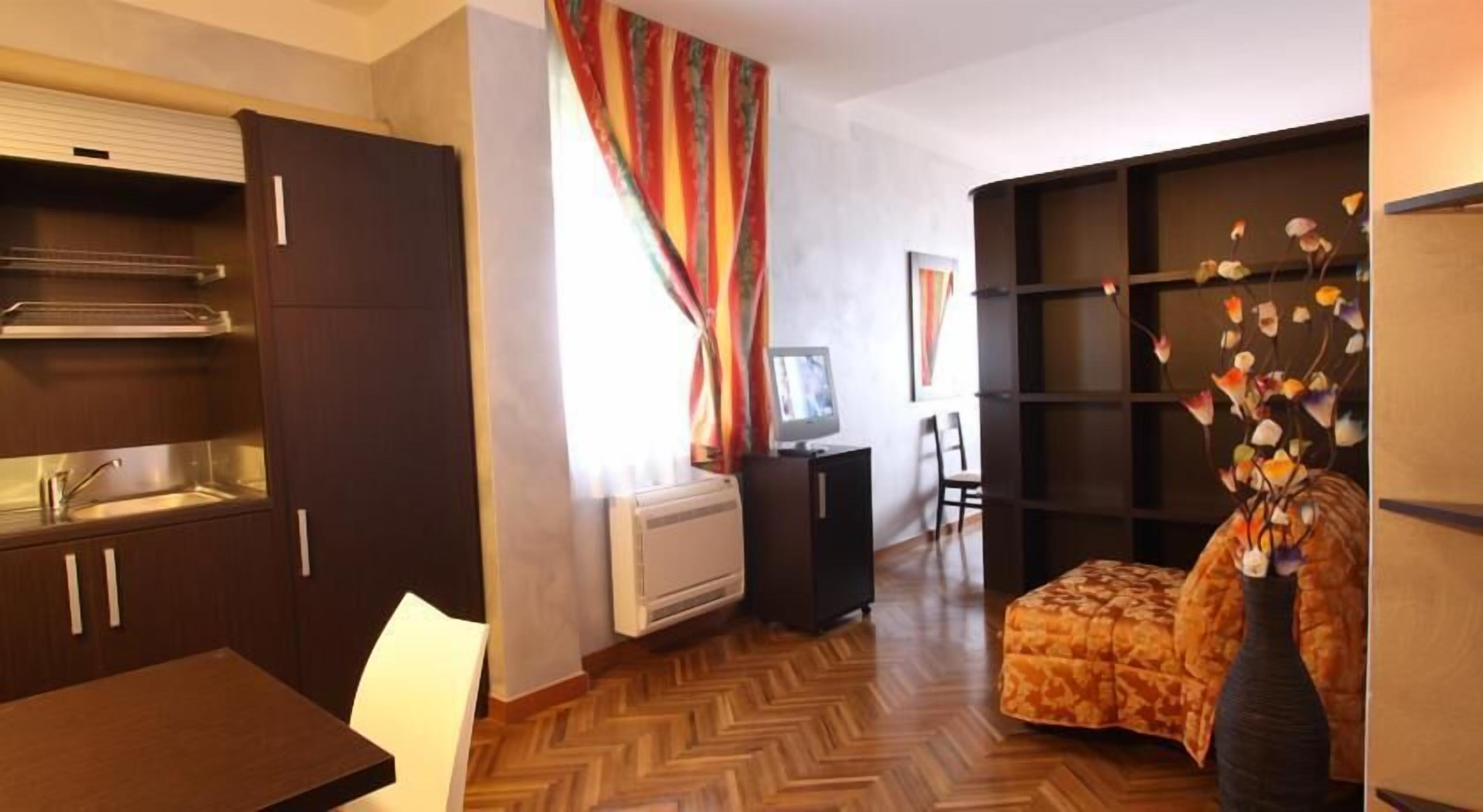 Un espacio habitable compacto con kitchenette, un sofá, un jarrón decorativo y un televisor.