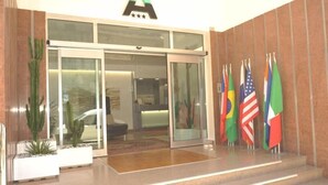 A hotel entrance with a glass door, a reception desk, and multiple flags. - Hotel Astoria (Fermo)