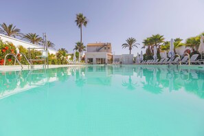 Ein Poolbereich mit Liegestühlen, Palmen und einem Gebäude im Hintergrund.