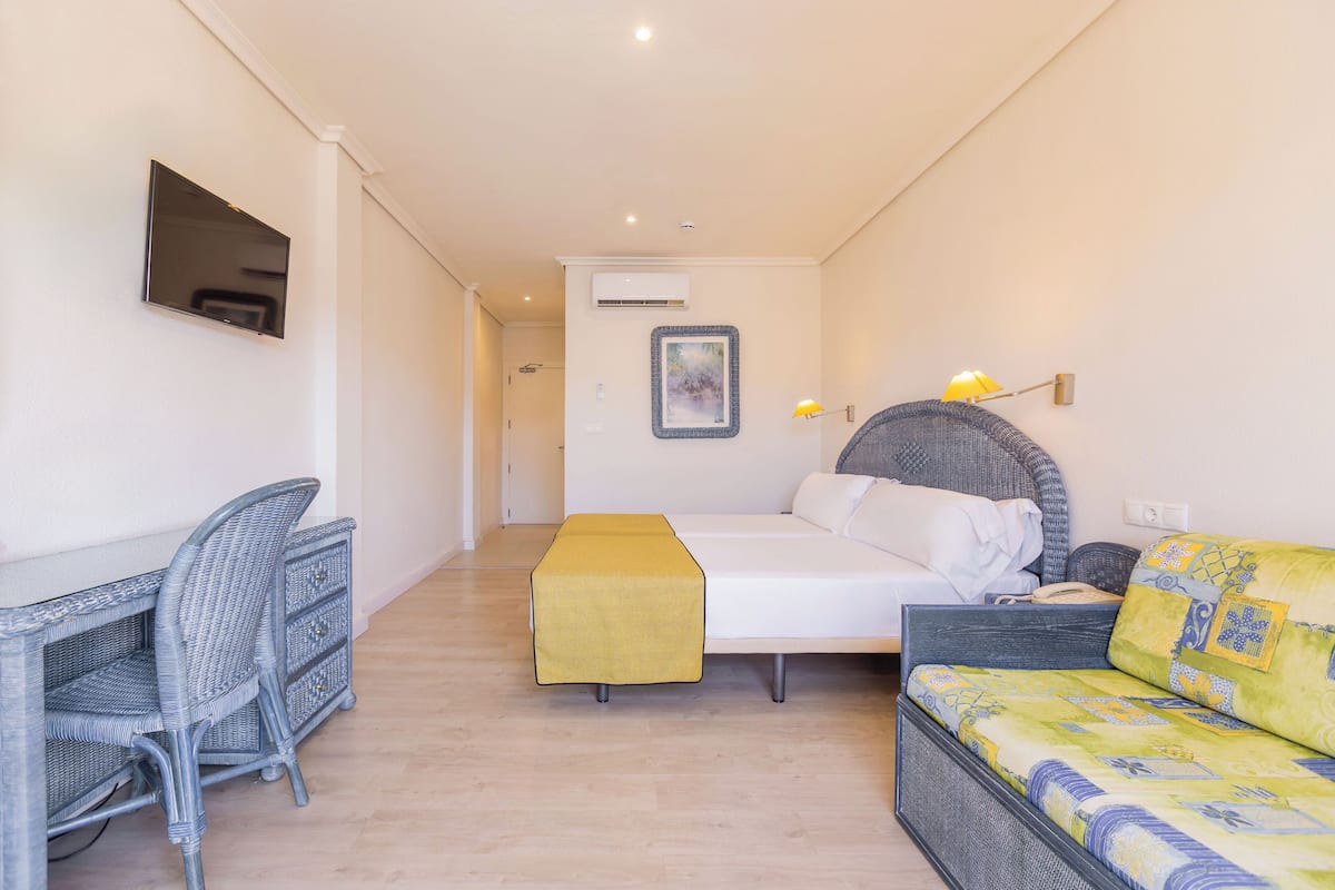 A bedroom with a bed, a desk, a chair, a sofa, and a wall-mounted TV.