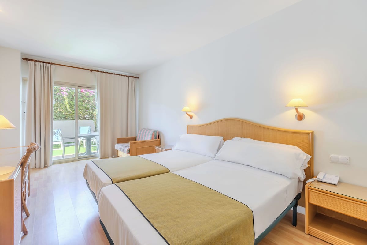 A hotel room with two beds, a balcony, a desk, and a chair.