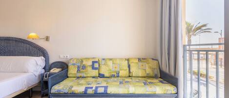 Una habitación con cama, sofá con cojines estampados, lámpara y vistas al exterior.