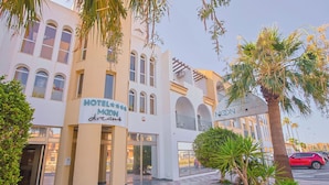 Un hôtel avec un sol à carreaux, des palmiers et une voiture rouge garée devant.