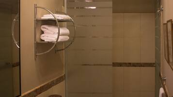 A bathroom with a granite countertop, a white toilet, a glass shower enclosure, and a chandelier.