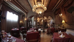 Un comedor formal con mesas dispuestas para el servicio, candelabros ornamentados y detalles arquitectónicos clásicos.