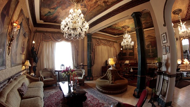 Una sala elegante con candelabros ornamentales, un sofá grande, un sillón redondo y una chimenea.