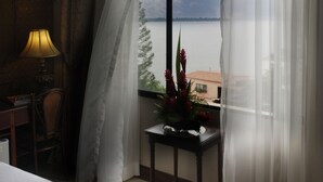 Una habitación de hotel con un ventanal grande, una mesita de noche con lámpara y vistas al mar.
