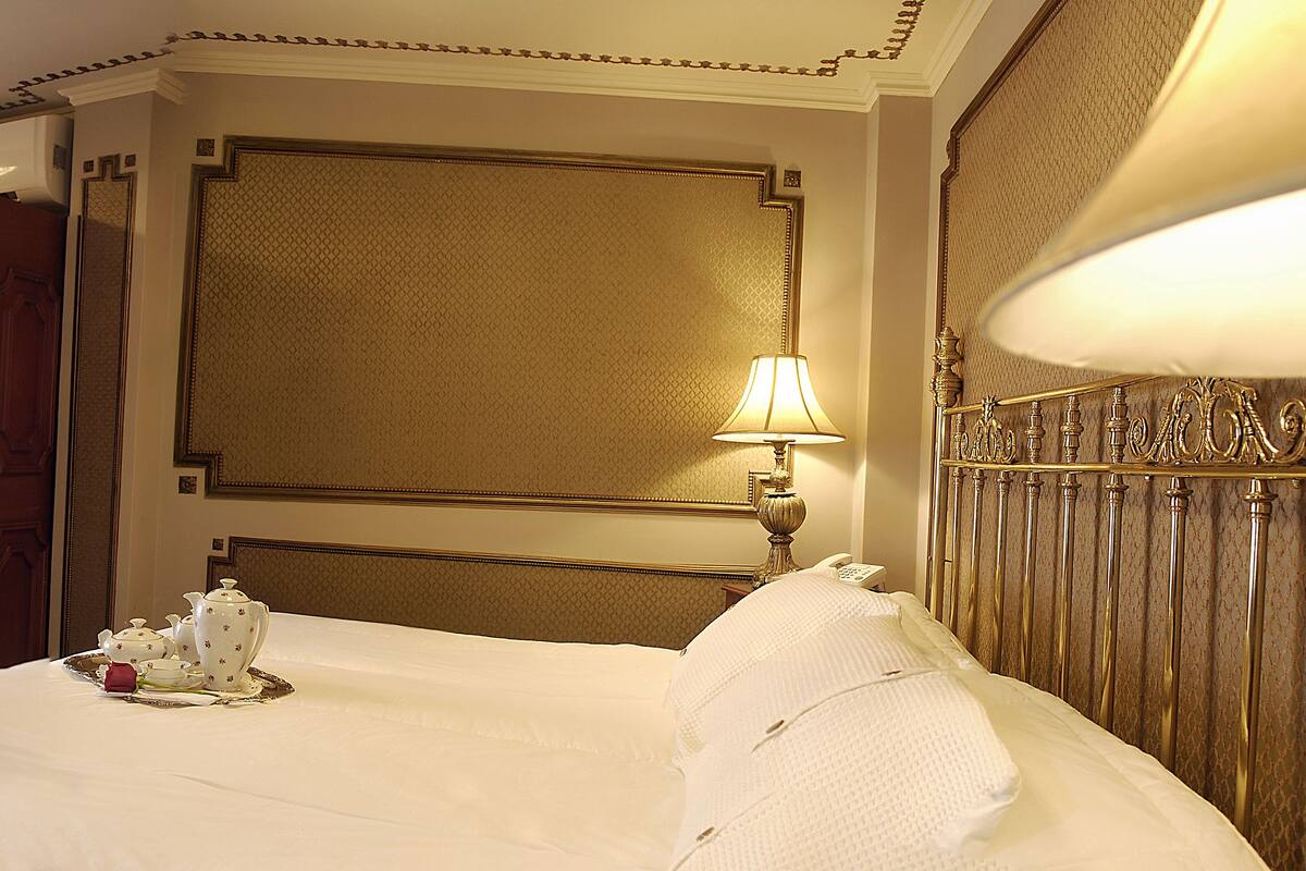 A hotel room with a large bed, a desk with a chair, a wardrobe, and a window with curtains.