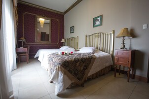 Habitación de hotel con dos camas, un escritorio, una silla, una mesita de noche, una lámpara, un espejo y cuadros en la pared.