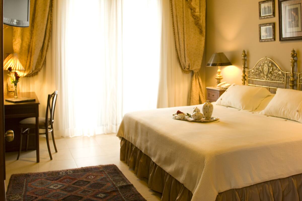 A hotel room with a large bed, a desk with a chair, a television, and a chandelier.