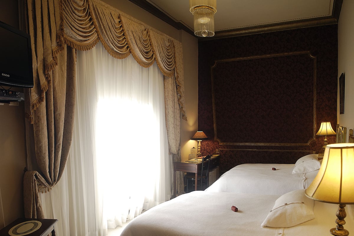 A hotel room with two beds, a desk, a chair, and a large window with curtains.