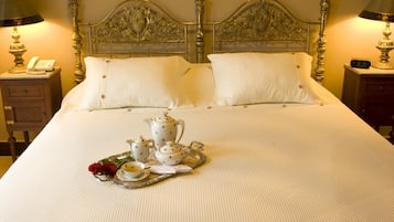 Una cama impecablemente arreglada con una bandeja de té y una rosa, una mesita de noche de madera con una lámpara y cuadros enmarcados en la pared.