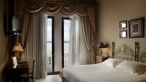Habitación de hotel con cama, escritorio con lámpara, televisión y vistas a través de las cortinas.