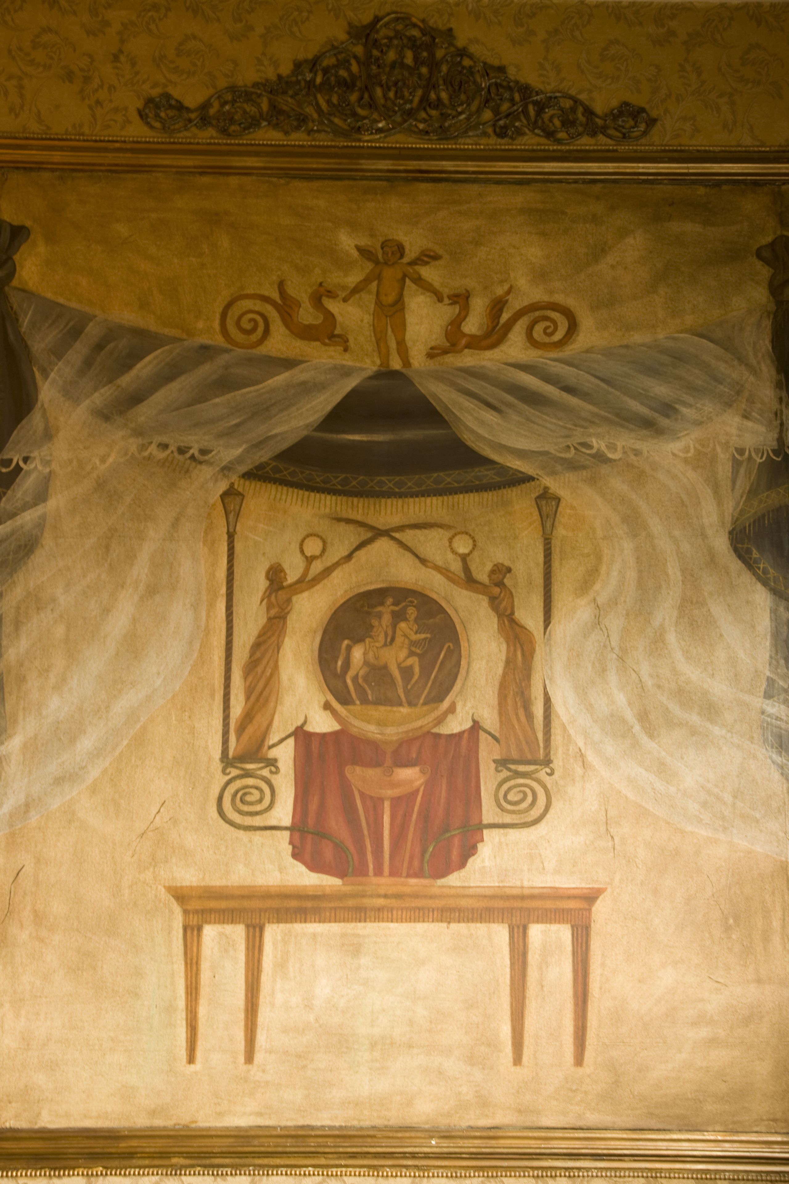 Un fresco en el techo con una figura central, cortinas y una mesa.