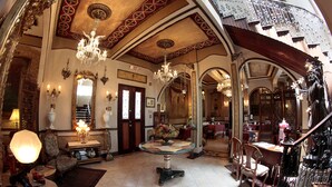 Una sala majestuosa con candelabros ornamentales, un espejo grande y una escalera que sube a otro nivel.