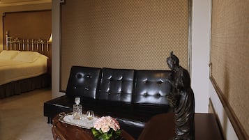 Una sala de estar con un sofá de cuero negro, una mesa de centro de madera con un jarrón de flores y una estatua en una mesita auxiliar.