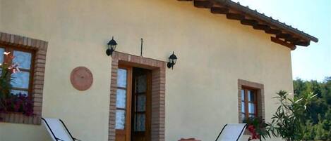 A building with a tiled roof, a door, and two chairs outside.