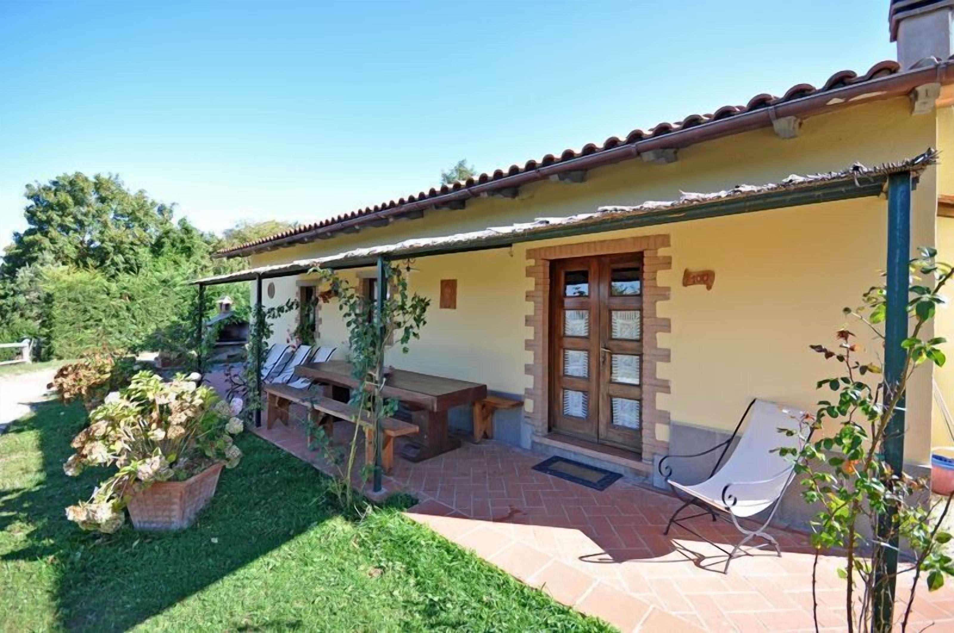 A covered patio with a wooden table and chairs, a small garden area with potted plants, and a door with a window.