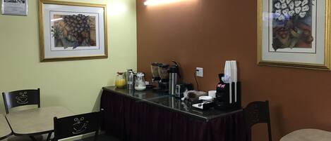 A conference room with a table, chairs, coffee-making equipment, and framed artwork on the walls.