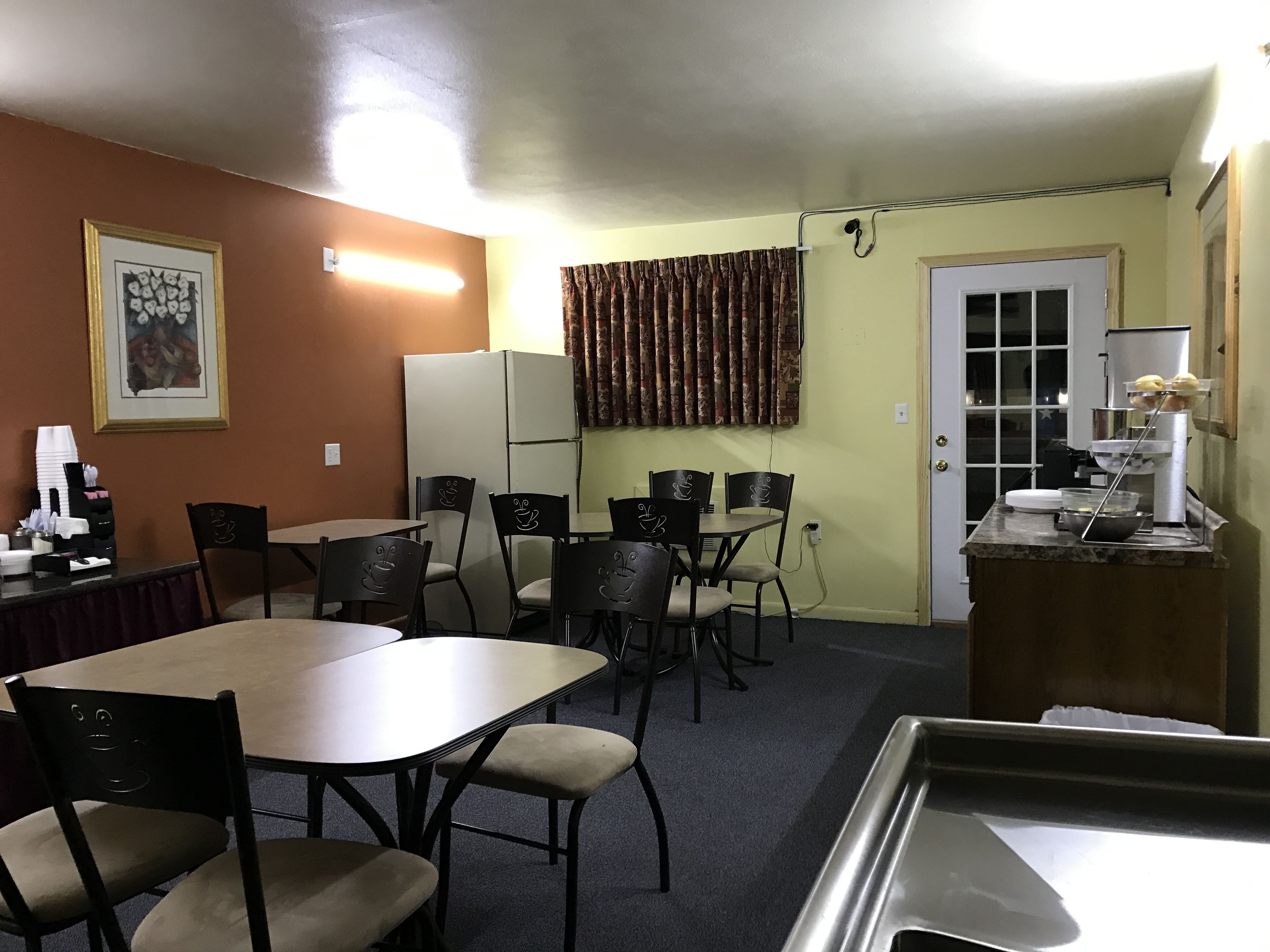 A dining area with a table and chairs, a refrigerator, a window with curtains, and a door.