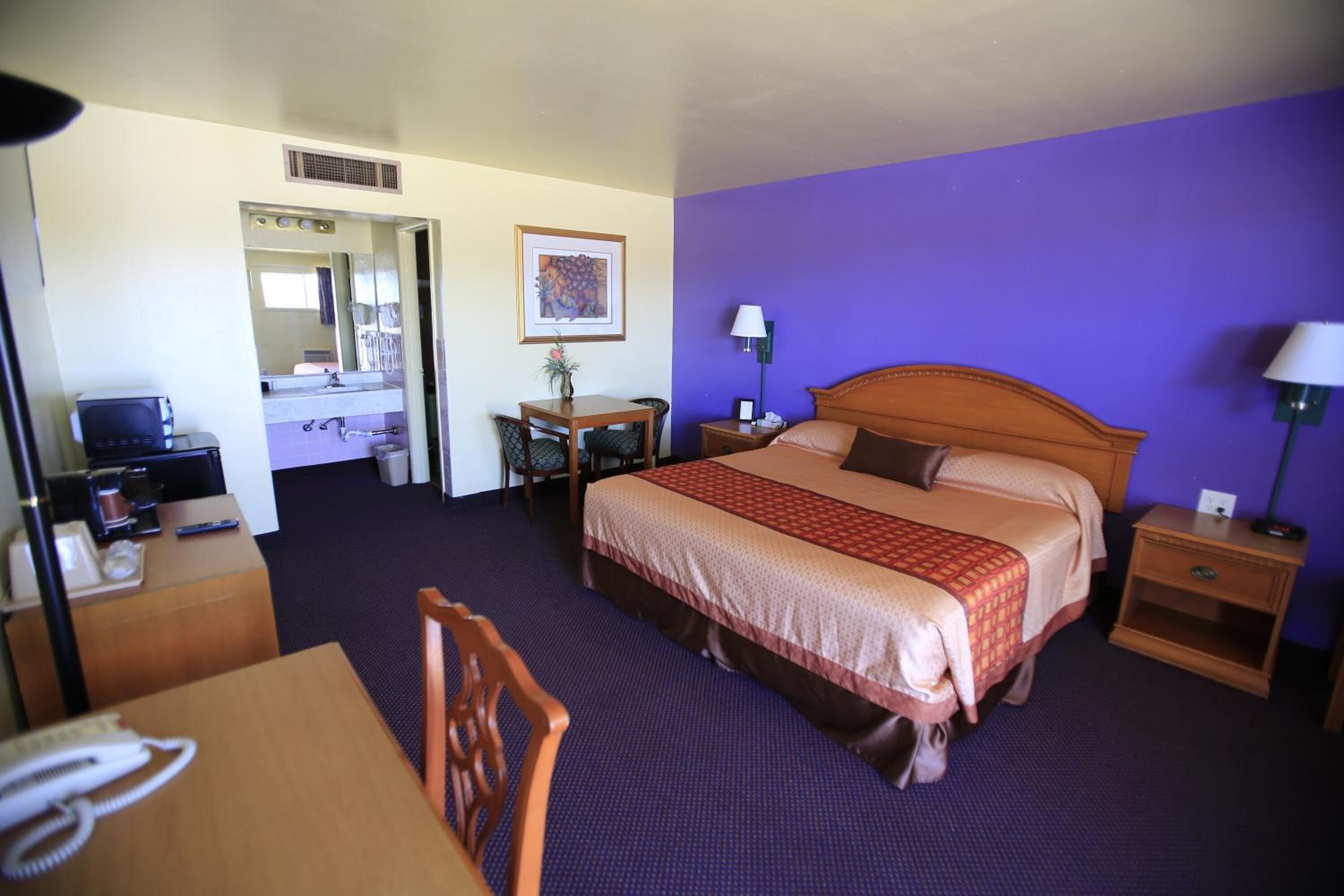 A hotel room with a bed, bedside tables, a desk with a chair, a mirror, and a bathroom visible through an open door.