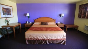 A hotel room with a large bed, two bedside tables, a desk with a chair, a framed picture on the wall, and a purple accent wall. - Shamrock Country Inn (Shamrock)