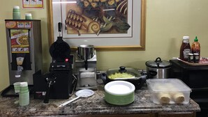 A kitchen counter with a waffle maker, a coffee machine, a pot, a bowl of food, and condiments. - Shamrock Country Inn (Shamrock)
