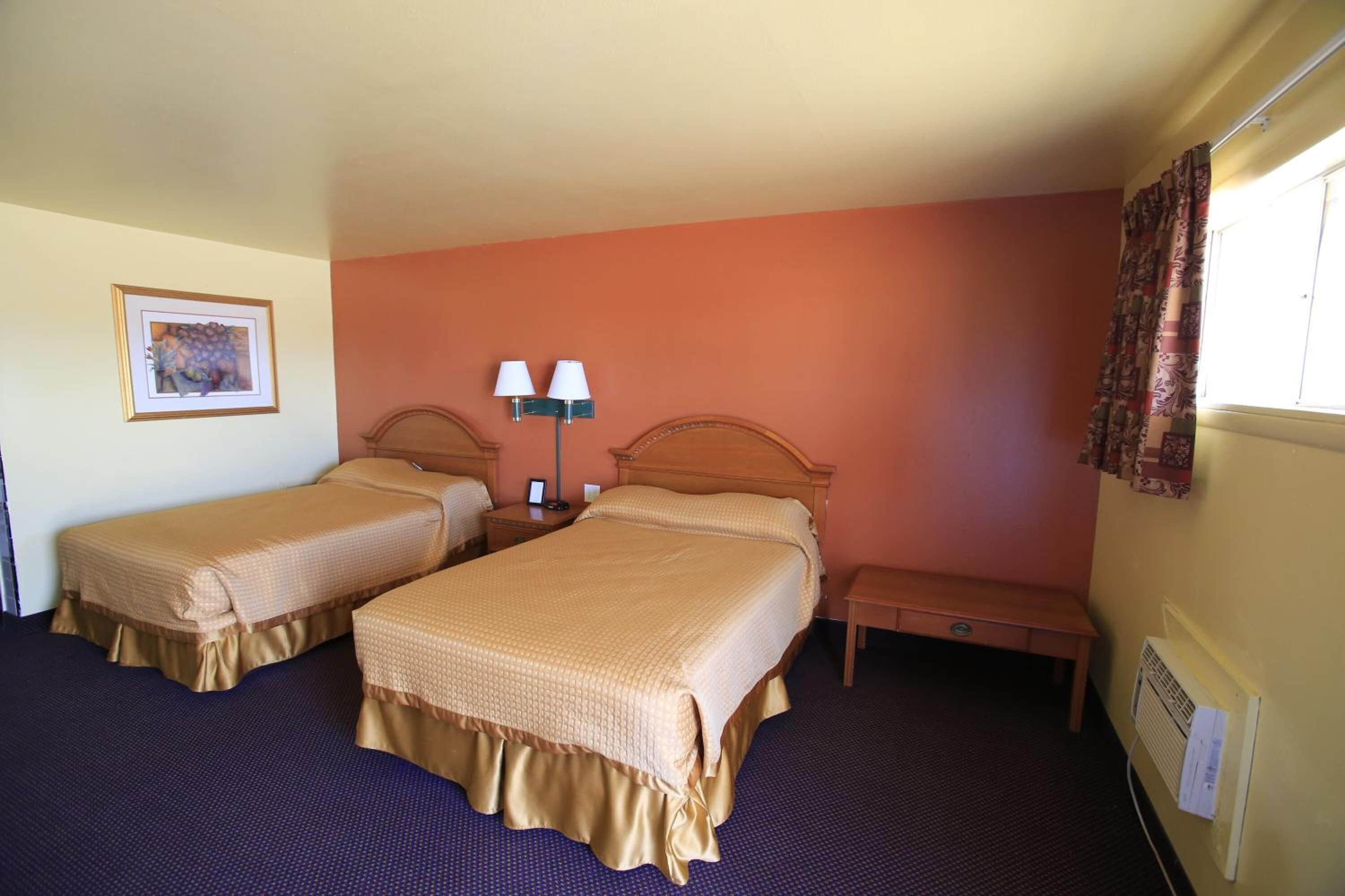 A hotel room with two beds, a nightstand with lamps, a bench, a framed picture on the wall, and a window with curtains.