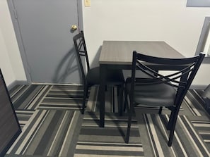 A room with a gray carpet, a gray wall, and a wooden table with two chairs. - Relax Inn (Saginaw)
