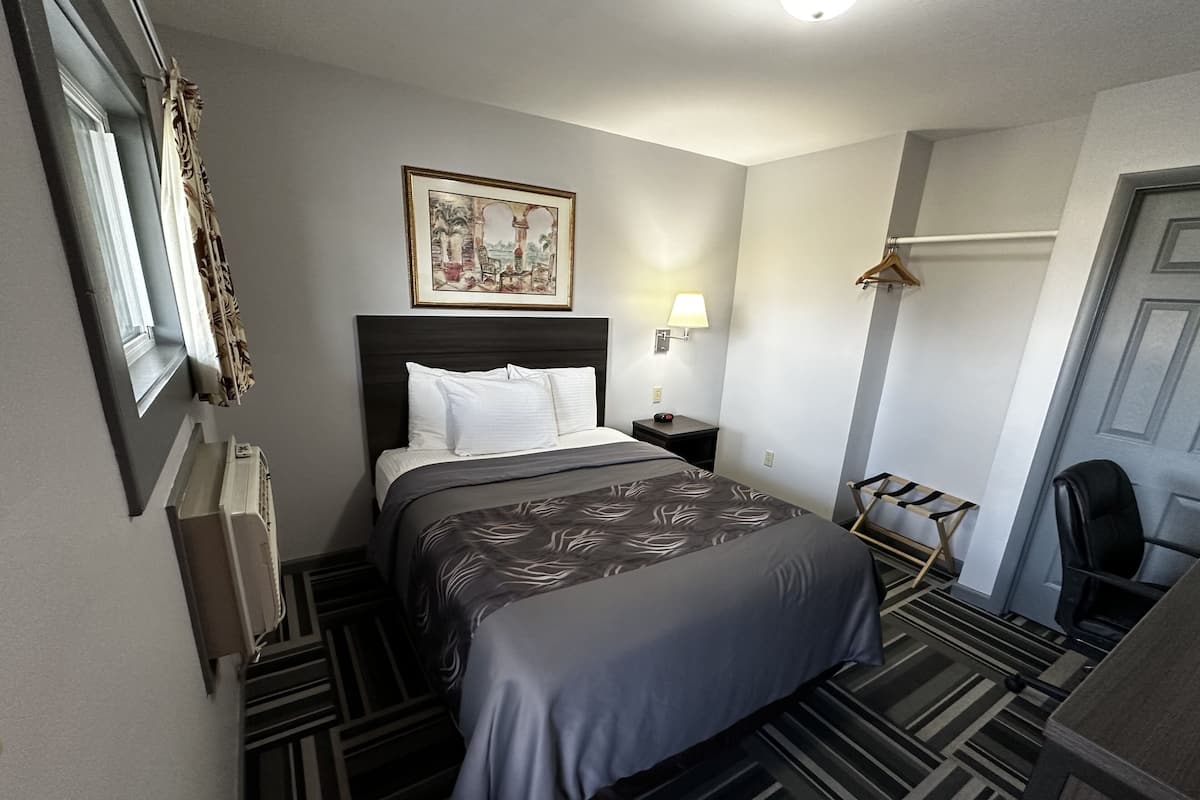 A hotel room with a bed, a nightstand, a lamp, a chair, and a door.