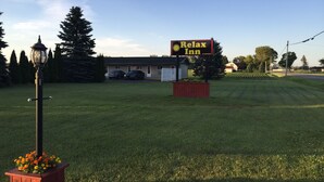 A sign for a Relax Inn with a lawn and a building in the background. - Relax Inn (Saginaw)