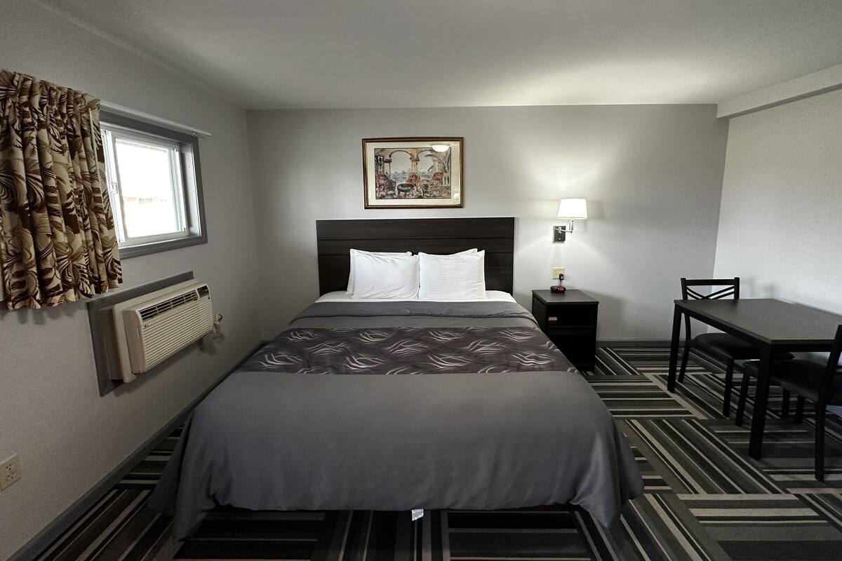 A hotel room with a bed, a desk, a chair, a picture on the wall, and a window with curtains.