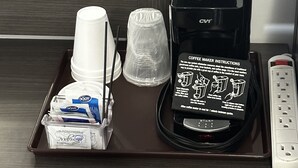 A coffee maker with instructions, disposable cups, a tray, and a remote control on a wooden table. - Relax Inn (Saginaw)