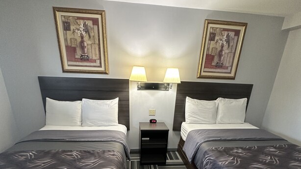 A hotel room with two beds, a nightstand, two wall-mounted lamps, and two framed pictures on the wall. - Relax Inn (Saginaw)