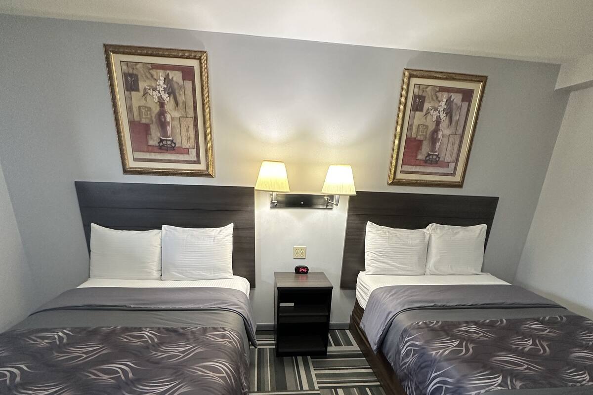 A hotel room with two beds, a nightstand, two wall-mounted lamps, and two framed pictures on the wall.