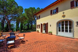 A patio with outdoor furniture and a building with a tiled roof and arched windows. - Villa Leonardo (Vinci)