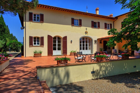 A two-story building with a tiled roof, a patio with outdoor furniture, and potted plants. - Villa Leonardo (Vinci)