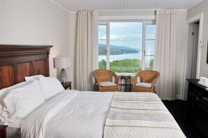 Habitación de hotel con una cama grande, dos sillones de mimbre, una mesita y vista a un lago a través de un ventanal amplio.